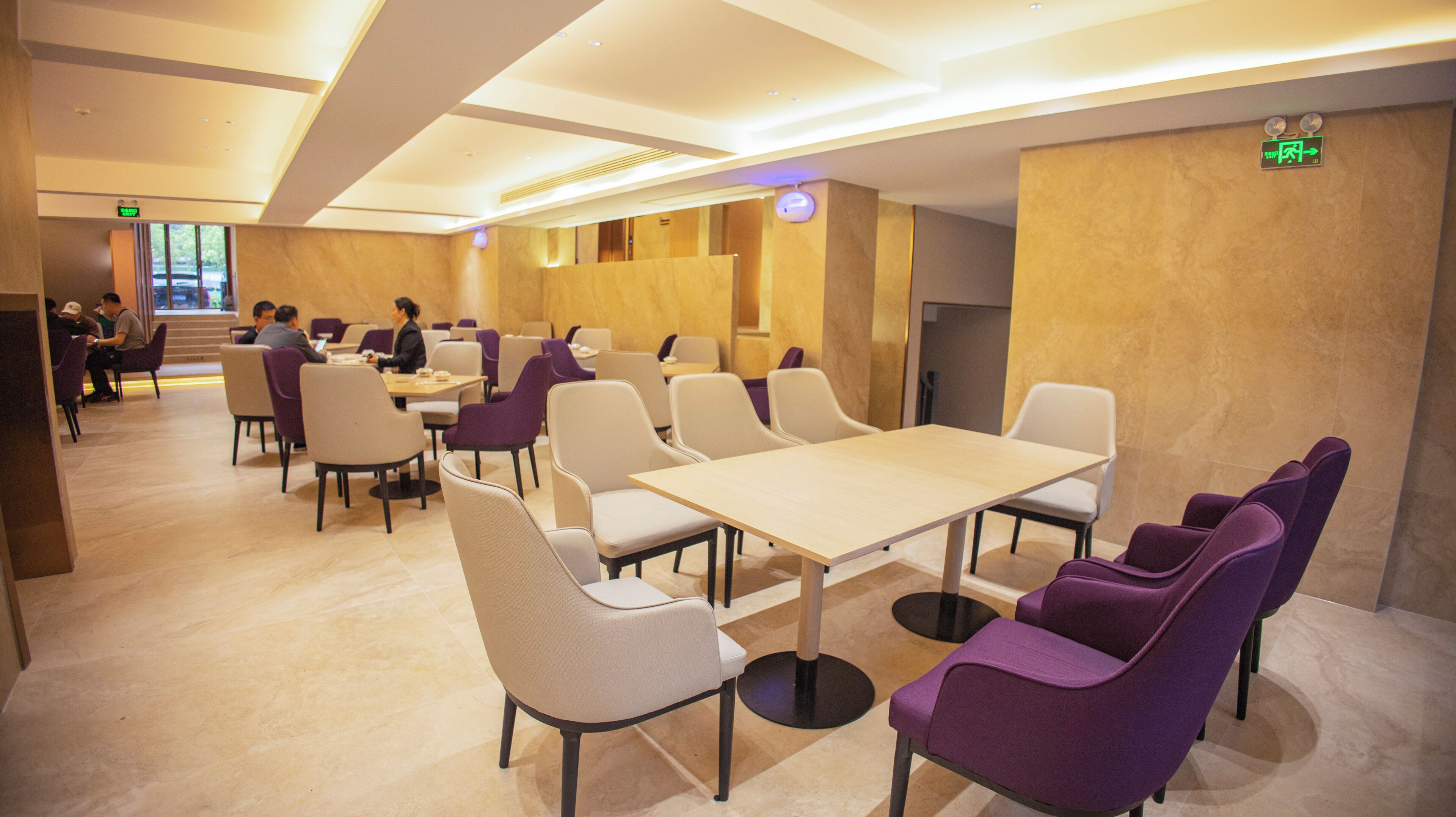 A modern hotel lobby with a seating area, tables, and a staircase leading to an upper floor.