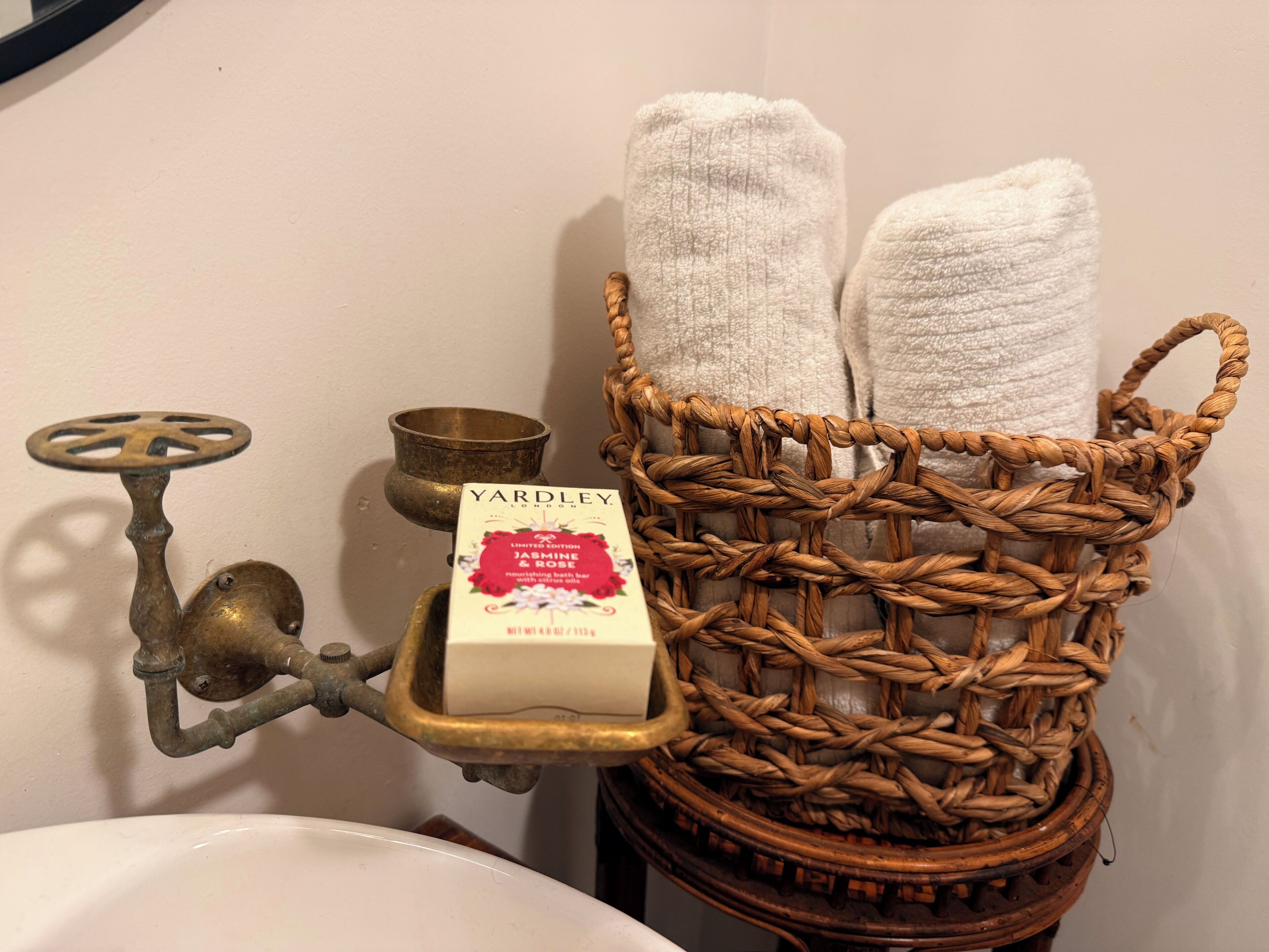 A bathroom with a brass faucet, a white sink, a wicker basket with towels, and a bar of Yardley London soap.