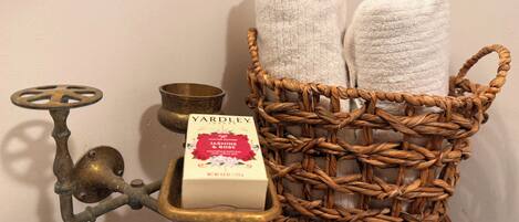 A bathroom with a brass faucet, a white sink, a wicker basket with towels, and a bar of Yardley London soap.