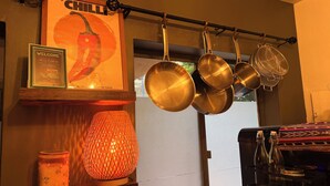 Eine Küche mit hängenden Töpfen, einer beleuchteten Lampe, einem gerahmten Schild und einem Regal mit einem Glas.