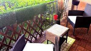 Ein Balkon mit Korbmöbeln, einem kleinen Tisch und einem roten Eimer.