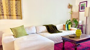 Ein weißes Sofa mit grün-weißen Kissen, ein Couchtisch aus Holz mit einer gelben Vase und ein gemustertes Teppich.