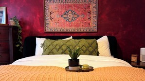 Ein Schlafzimmer mit Bett, Kopfstütze, Nachttisch, Blumentopf, Teppich unter Glas und Wandheizung.