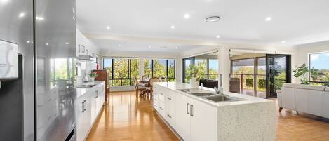A modern kitchen with a large island, wooden flooring, and a view of the outdoors.
