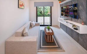 Una sala de estar moderna con un sofá, una mesa de centro, un televisor montado en la pared y un ventanal corredero que da a un espacio exterior.