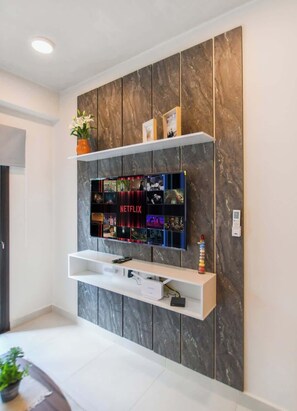 Una sala de estar moderna con un televisor de pantalla plana montado en una pared de textura similar al mármol. Hay estantes arriba y debajo del televisor, con una planta en maceta en el estante superior.