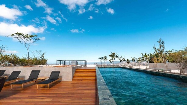 Una piscina sul tetto con pavimento in legno e poltrona relax, immersa nel verde e sotto un cielo sereno.