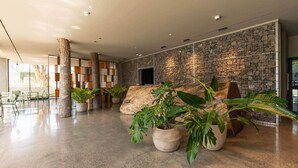 Un'ampia hall con pavimento in cemento lucidato, grandi piante in vaso e una parete in pietra con motivo a griglia.