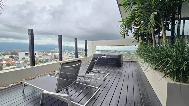 Eine Dachterrasse mit zwei Liegestühlen, einem Grill und Blick auf die Skyline.