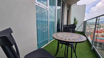 A balcony with a round table and two chairs, a view of the city, and a glass door.
