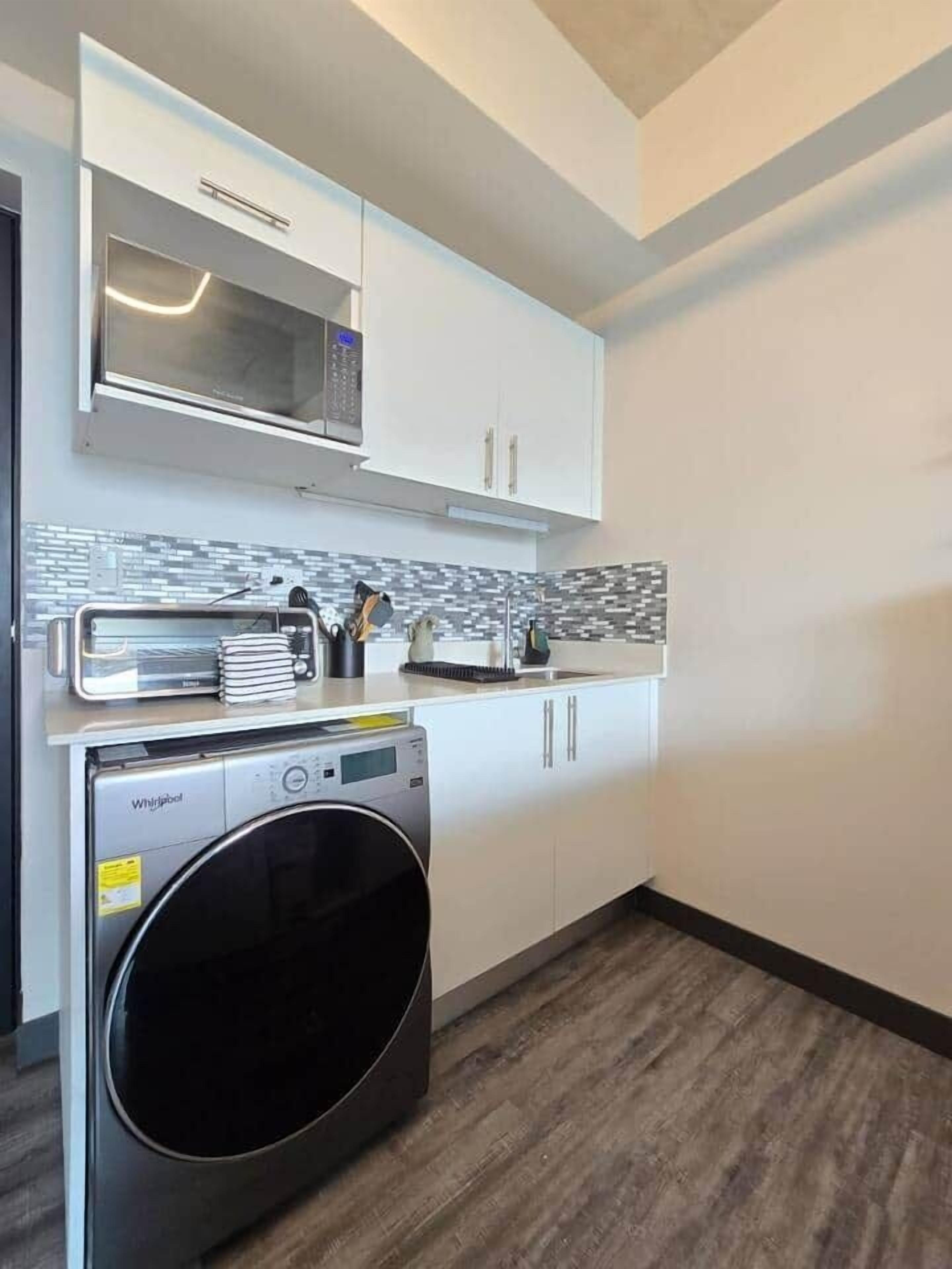 A compact kitchen with a built-in microwave, a washing machine, and a tiled backsplash.
