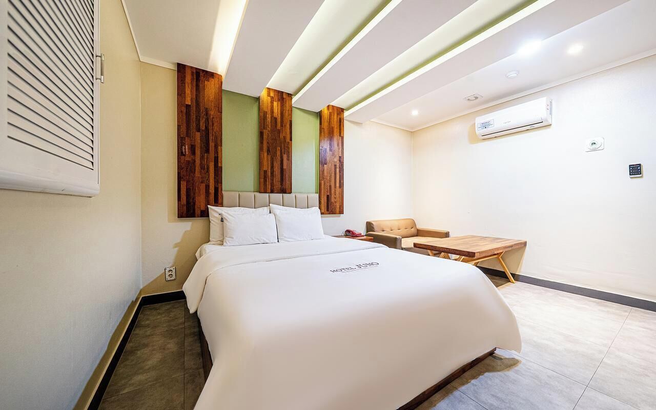 Ein Hotelzimmer mit Bett, kleinem Tisch, Stuhl und Wandklimaanlage.