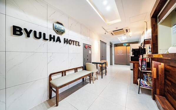 A BYULHA HOTEL reception area with a marble wall, a bench, chairs, a reception desk, and a vending machine.