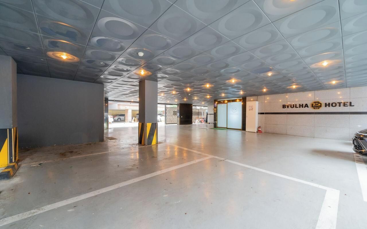 A modern hotel lobby with a distinctive ceiling design, a BYULHA HOTEL sign, and a clean, spacious floor layout.