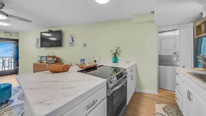 A modern kitchen with a built-in oven, a large island, and a dining area with a blue chair. - Renovated Beachfront Studio | Private Balcony, Pool & Direct Beach Access | $300 Free Fun Included (Panama City Beach)