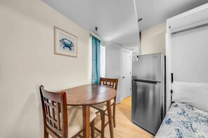 A compact room with a dining table, chairs, a bed, a refrigerator, and a door leading to another room. - Renovated Beachfront Studio | Private Balcony, Pool & Direct Beach Access | $300 Free Fun Included (Panama City Beach)