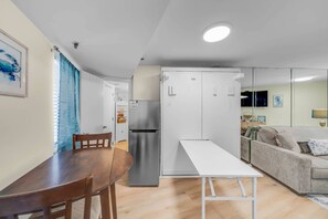 A compact living space with a dining table, chairs, a refrigerator, a sofa, and a white cabinet. - Renovated Beachfront Studio | Private Balcony, Pool & Direct Beach Access | $300 Free Fun Included (Panama City Beach)