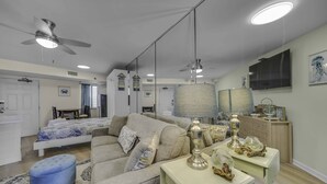 A modern living room with a sofa, a coffee table, a TV, and a ceiling fan. - Renovated Beachfront Studio | Private Balcony, Pool & Direct Beach Access | $300 Free Fun Included (Panama City Beach)