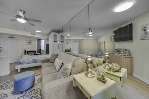A modern living room with a sofa, a coffee table, a TV, and a ceiling fan. - Renovated Beachfront Studio | Private Balcony, Pool & Direct Beach Access | $300 Free Fun Included (Panama City Beach)