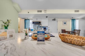 A modern kitchen with white cabinets, a microwave, and a dining area with a table and chairs. - Renovated Beachfront Studio | Private Balcony, Pool & Direct Beach Access | $300 Free Fun Included (Panama City Beach)