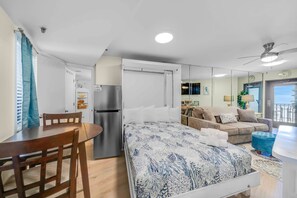 Quarto de hotel compacto com cama, mesa de jantar, cozinha compacta, sofá e varanda.