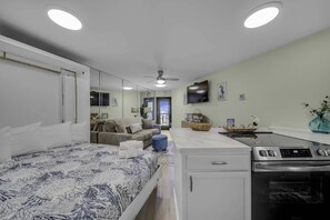 A modern hotel room with a bed, kitchenette, ceiling fan, and a view of the outside. - Renovated Beachfront Studio | Private Balcony, Pool & Direct Beach Access | $300 Free Fun Included (Panama City Beach)