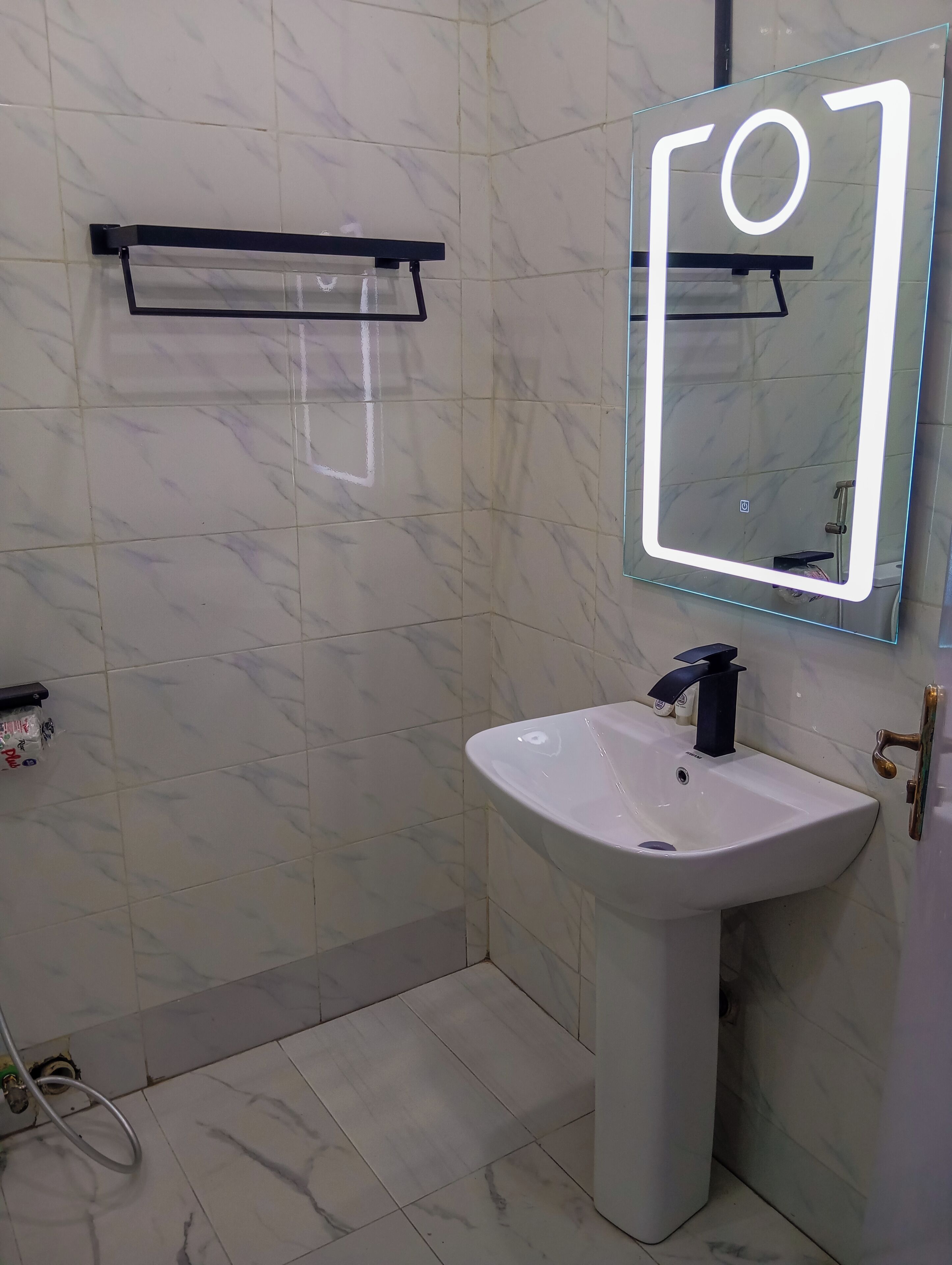 Un baño con lavamanos blanco, un espejo con luz y un perchero para toallas.