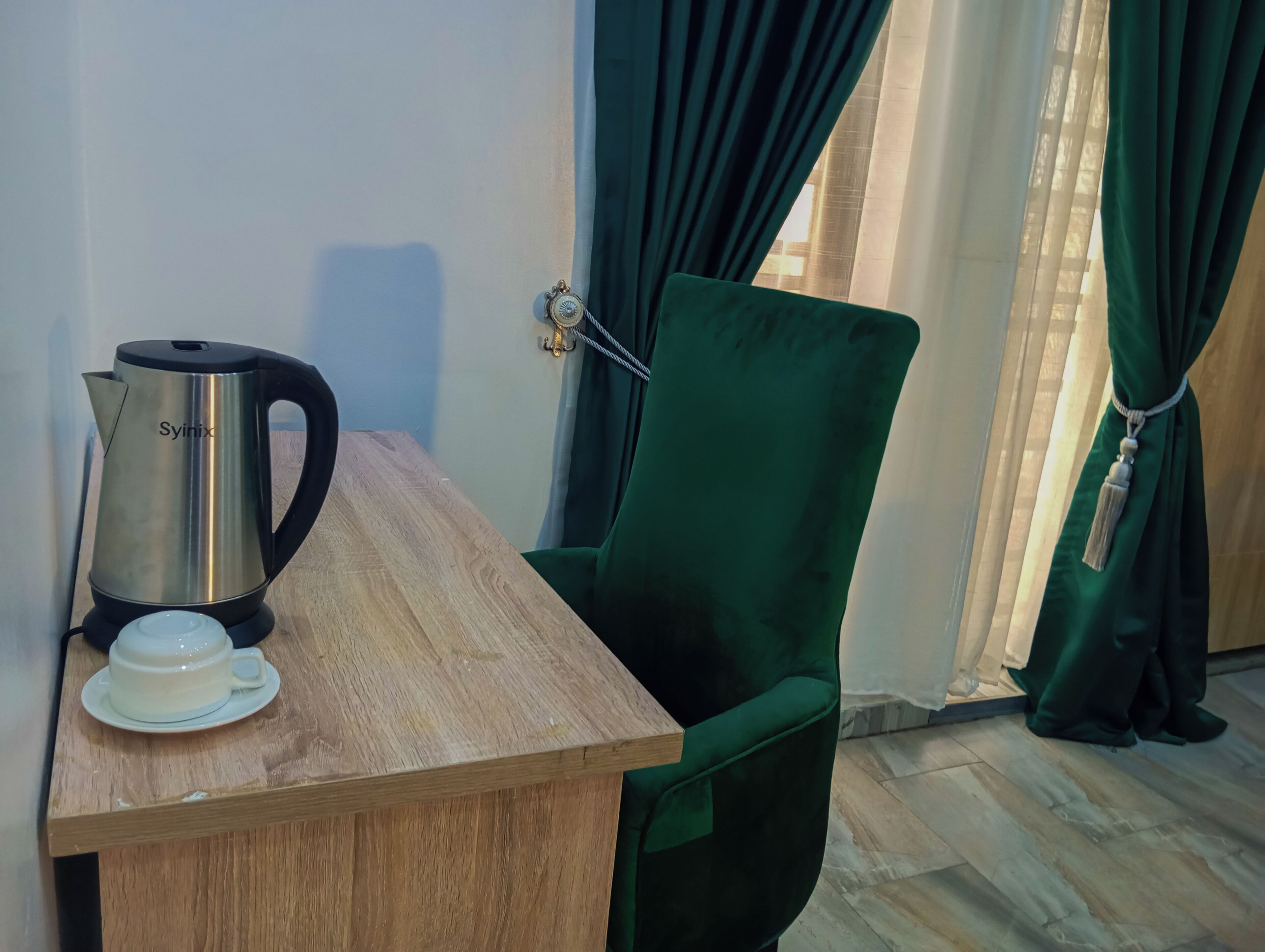 Une pièce avec une table en bois, une chaise verte, une bouilloire et une tasse.