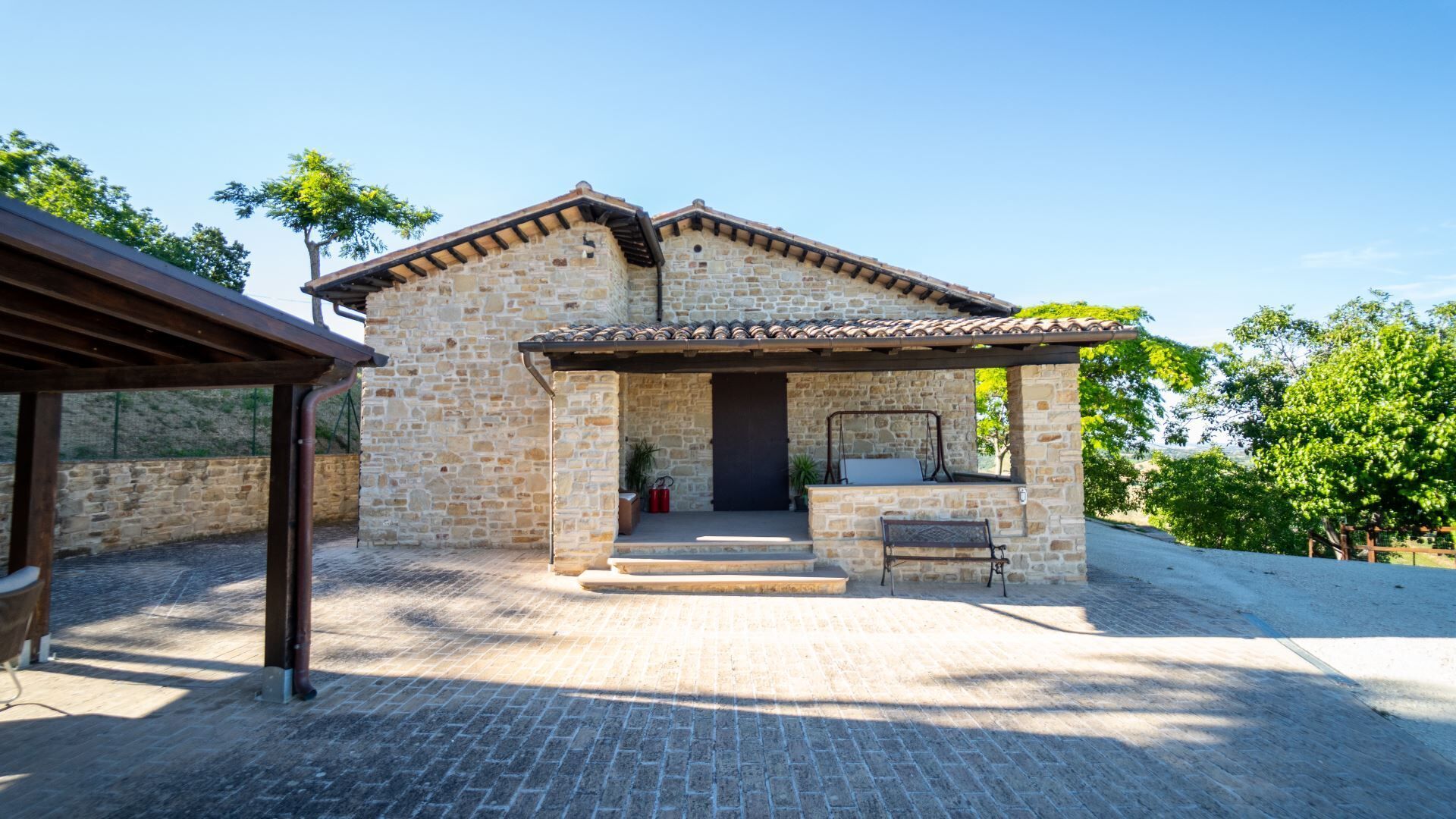 A stone building with a tiled roof, a covered patio, and a bench.