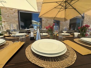 Een terras met eettafels gedekt voor twee personen, met geweven placemats, witte borden en glazen.