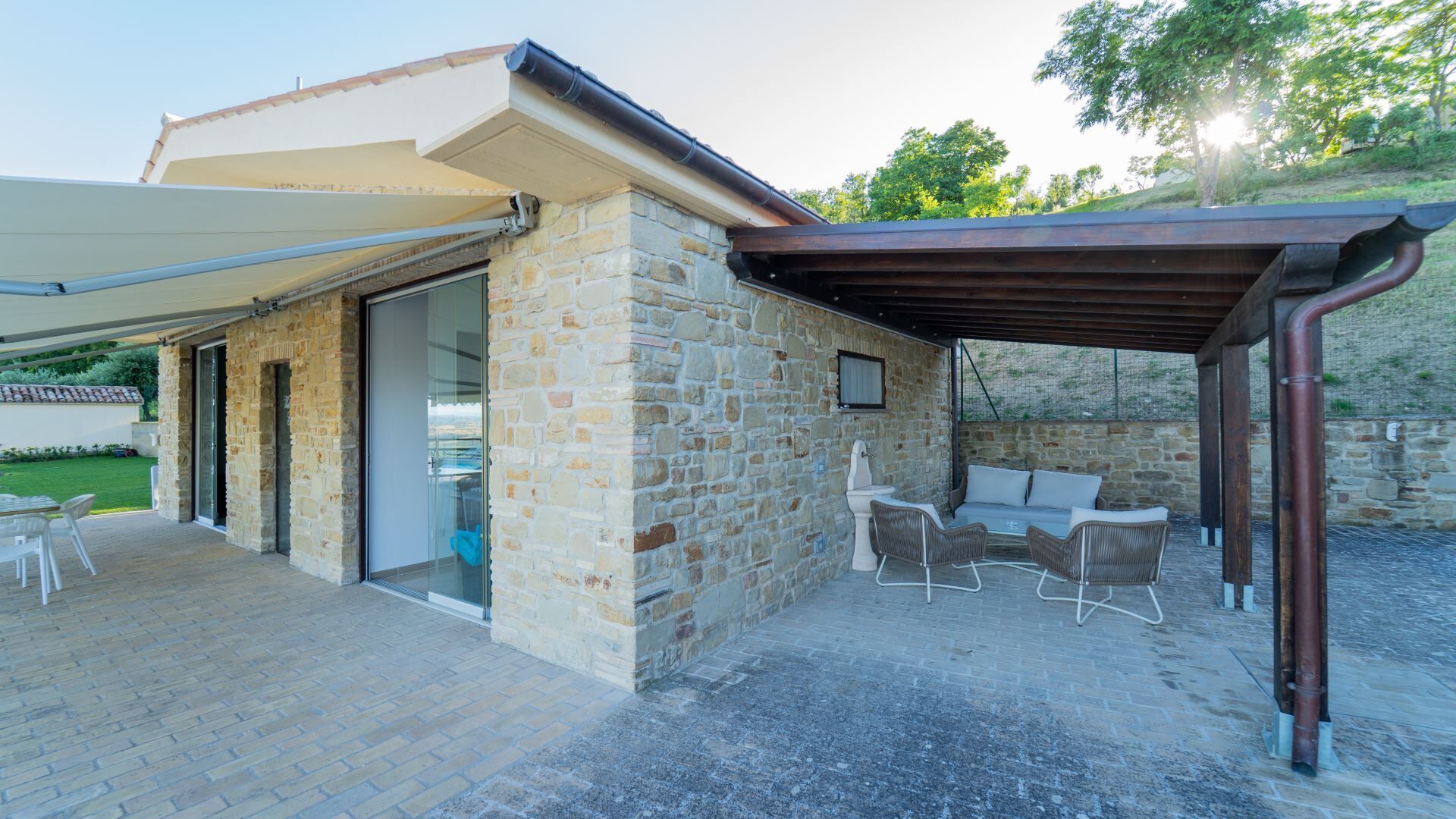Een stenen gebouw met een overdekt terras, buiten zitplaatsen en een pergola.