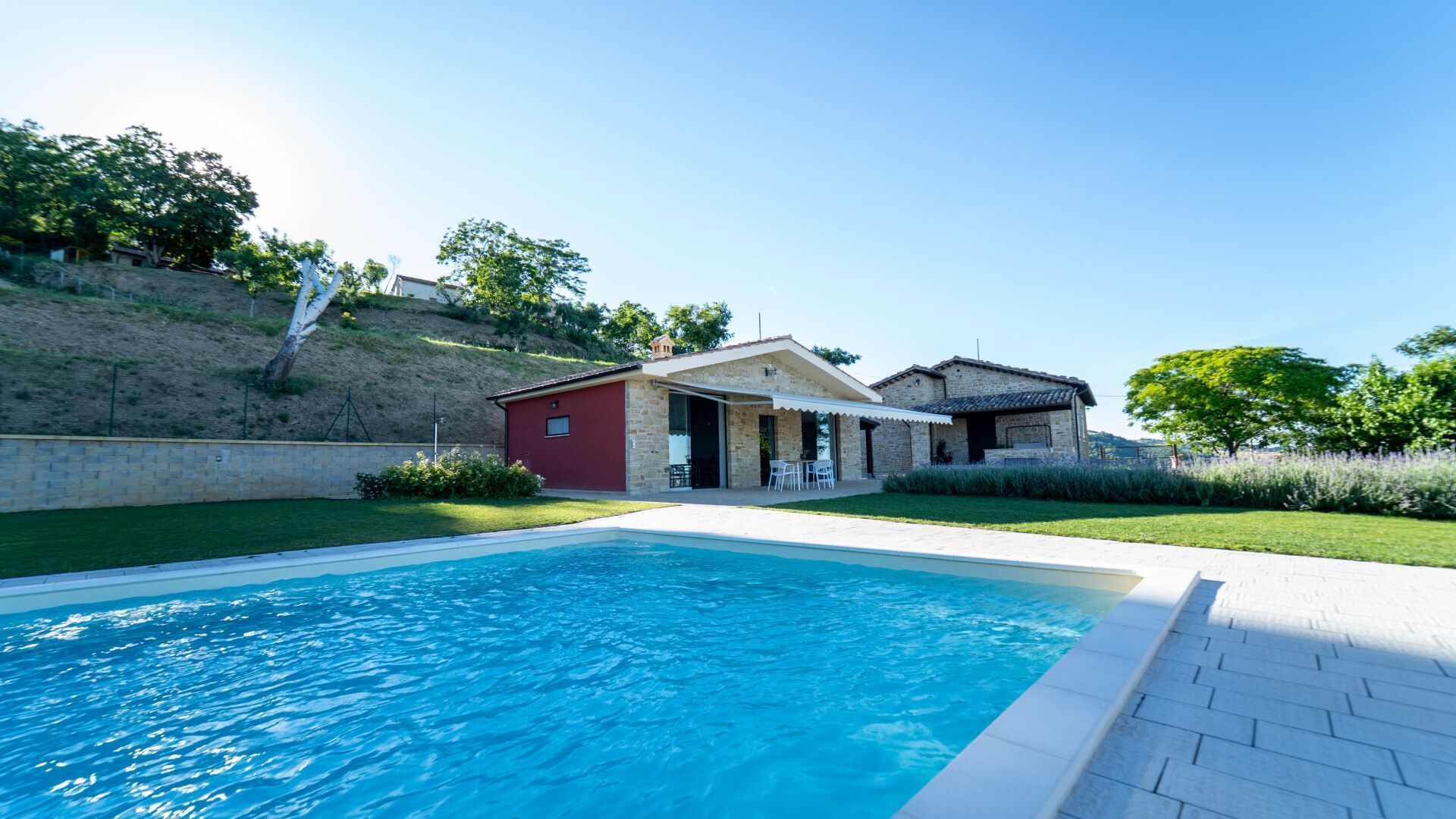 A swimming pool with a patio area, a red building, and a stone house with a tiled roof.