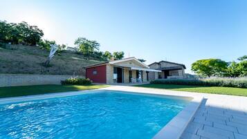 A swimming pool with a patio area, a red building, and a stone house with a tiled roof.