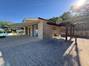 A stone building with a covered patio, outdoor seating, and a pool.