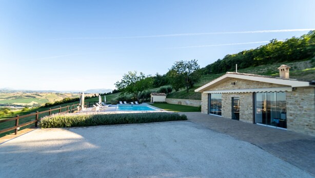 Zona de piscina con vistas al campo, un edificio de piedra con puerta de cristal y una valla de madera.