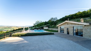 A pool area with a view of the countryside, a stone building with a glass door, and a wooden fence.