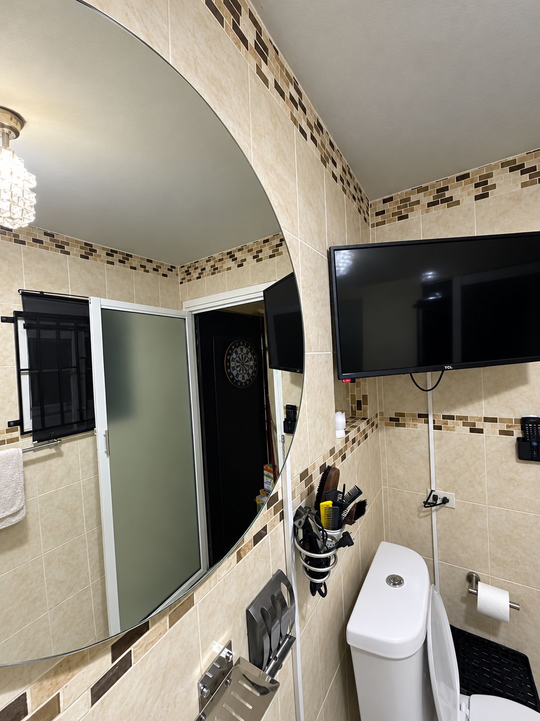 Une salle de bain équipée de toilettes, d’un lavabo, d’un miroir et d’un téléviseur fixé au mur.