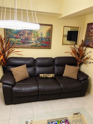 A black leather sofa with two decorative pillows, a chandelier, and framed artwork on the walls. - Jamaica R Home (Kingston)