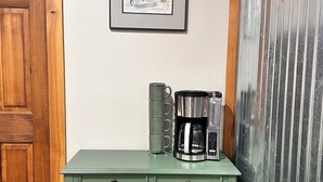 Un mueble verde de madera con un cuadro enmarcado encima, una cafetera y una taza sobre la encimera.