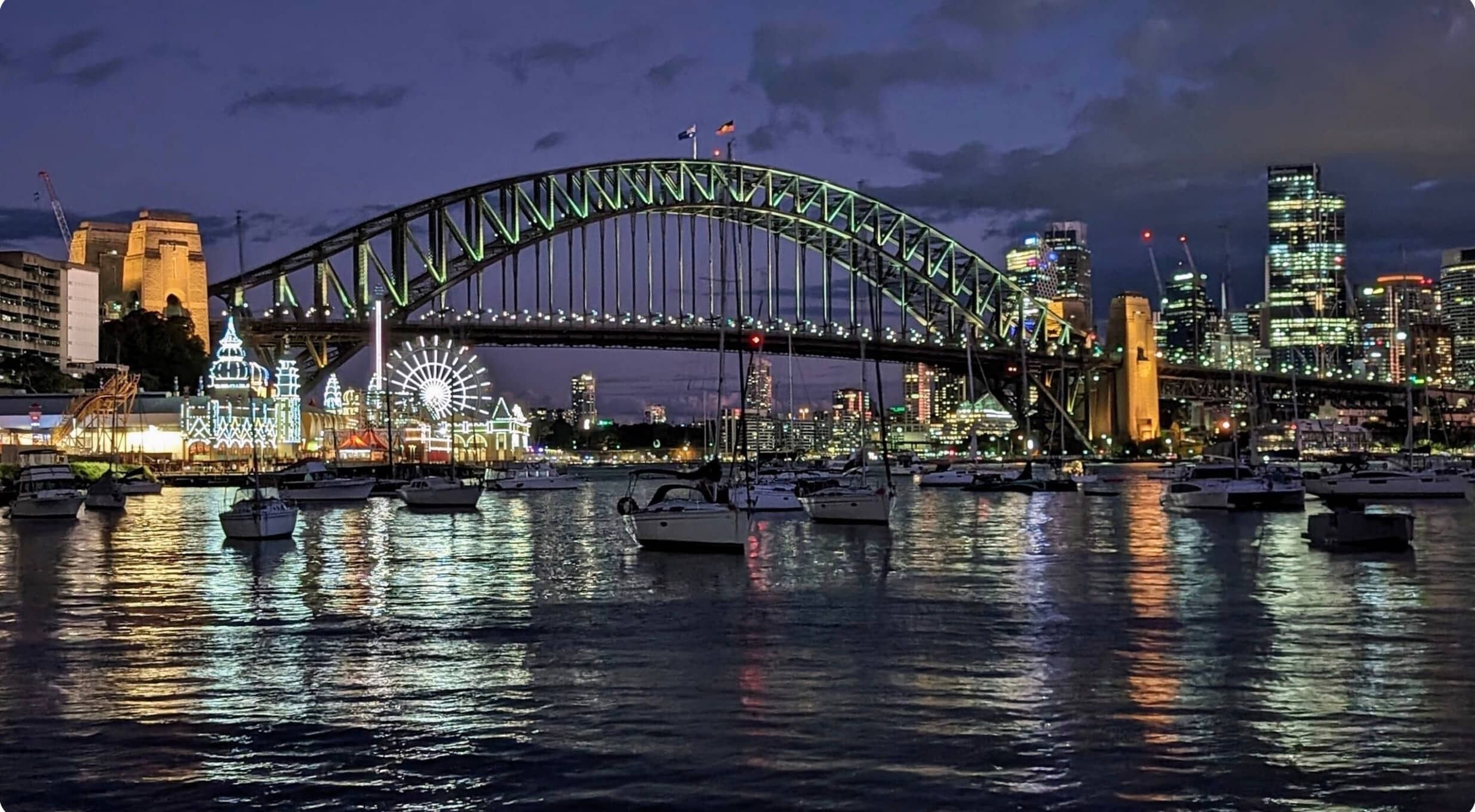 A nighttime view of a cityscape with a prominent bridge, waterfront, and illuminated buildings.