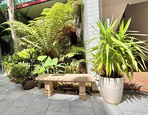 A bench in a garden area with various potted plants and a white brick wall. - Stylish 2BR City Escape next Harbour and 2 parking (Woolloomooloo)