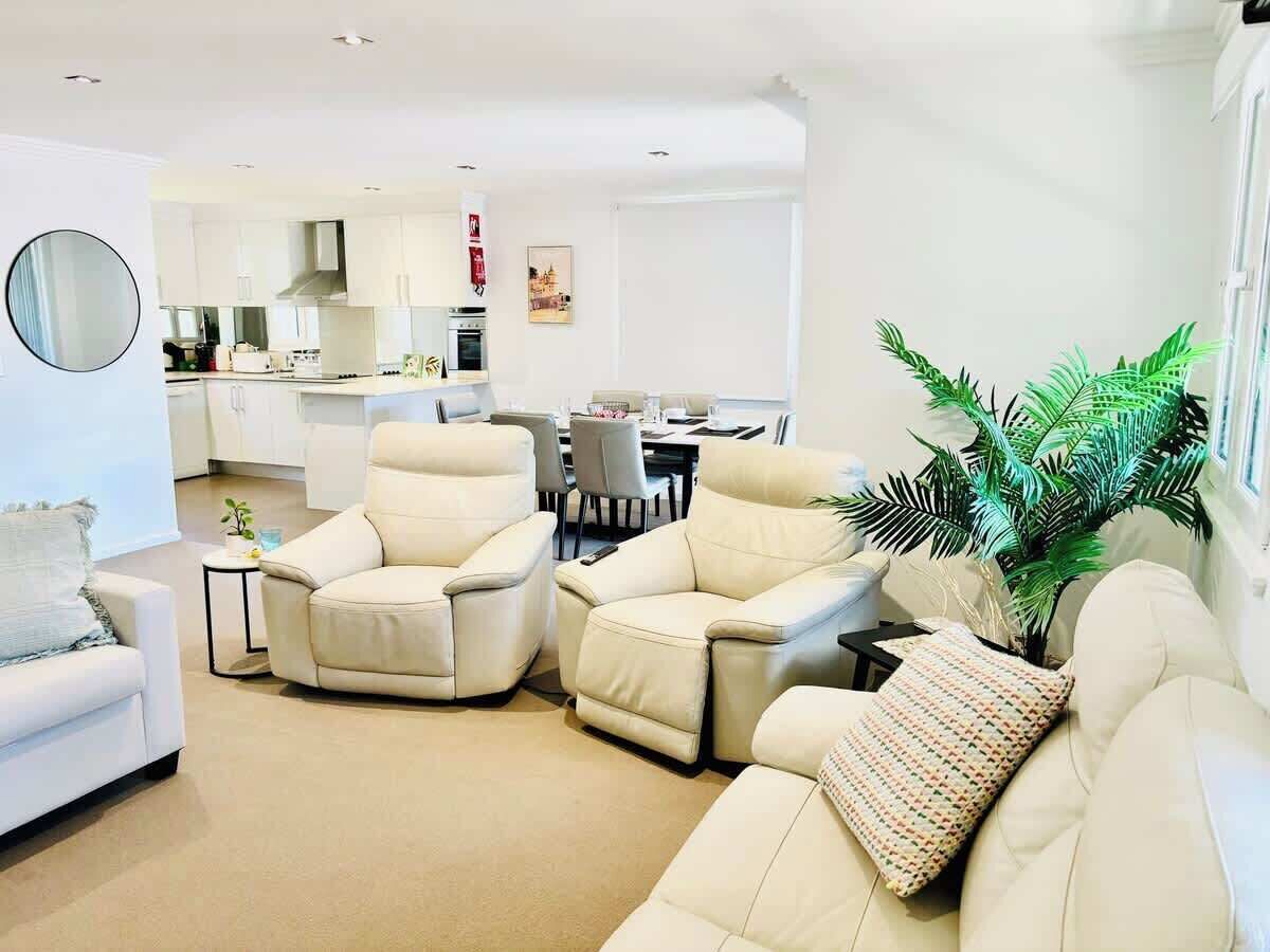 A modern living room with a sofa, two armchairs, a small side table, and a large potted plant.