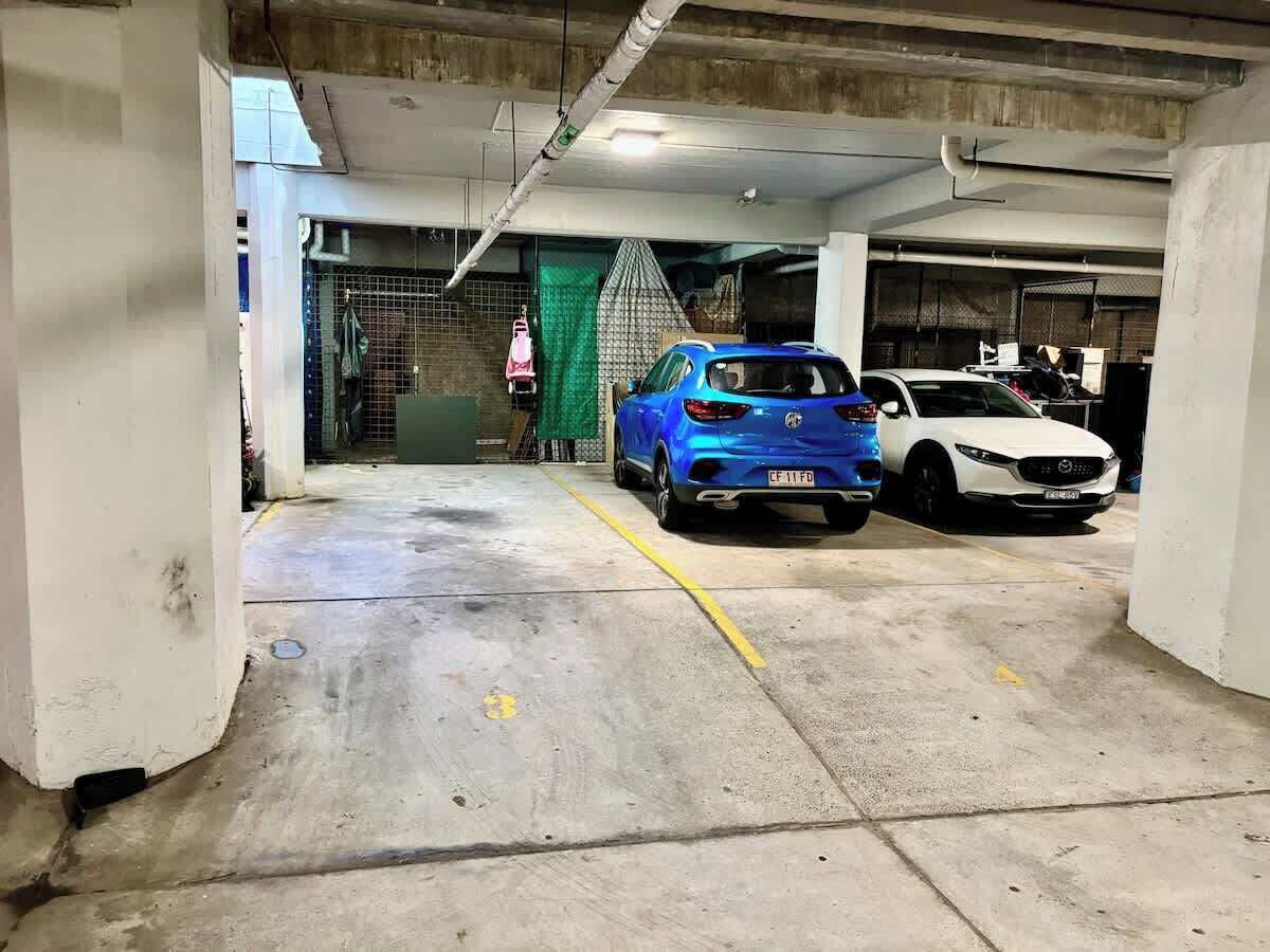 A parking garage with concrete floors, a blue car, and a white car parked.