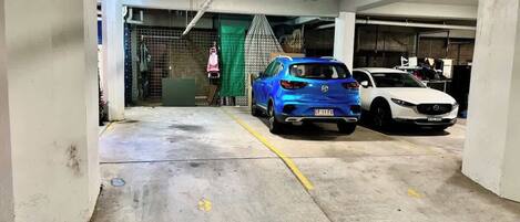 Un parcheggio sotterraneo con pavimenti in cemento, un'auto blu e un'auto bianca.