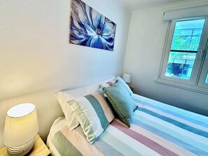 A bedroom with a bed, pillows, a bedside lamp, a window, and a wall painting. - Stylish 2BR City Escape next Harbour and 2 parking (Woolloomooloo)