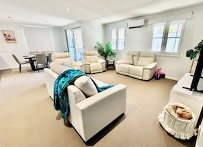 A spacious living room with a sofa, armchairs, a dining table, and a large window. - Stylish 2BR City Escape next Harbour and 2 parking (Woolloomooloo)