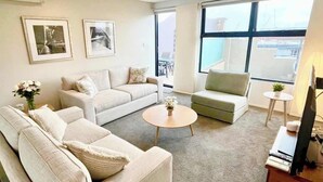 Ein modernes Wohnzimmer mit einem beigen Sofa, einem runden Couchtisch und einem Fernseher auf einem Holzboden.