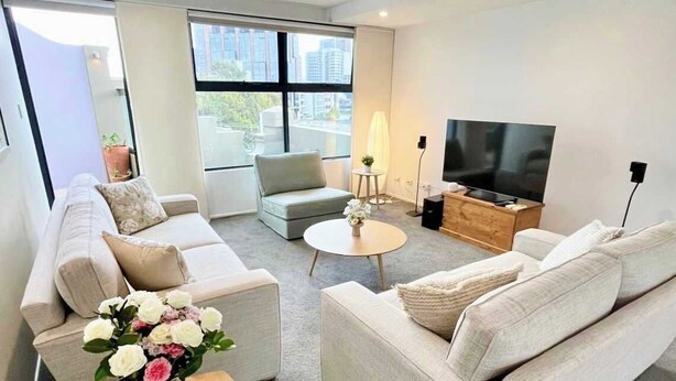 Ein modernes Wohnzimmer mit einer Sofagarnitur, einem Couchtisch, einem Fernseher und einem großen Fenster.