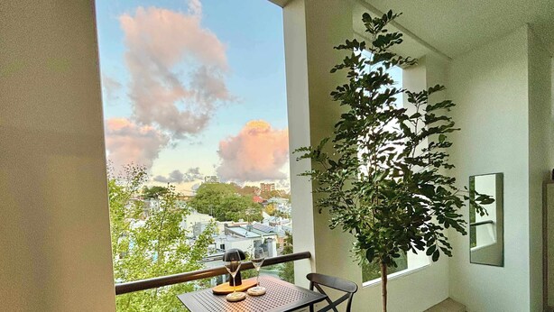 Un balcón con una mesa, sillas, una planta en maceta y vistas de la ciudad.