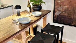 Comedor con una mesa de madera, dos sillas negras, una planta en maceta, una botella de vino y un bol.